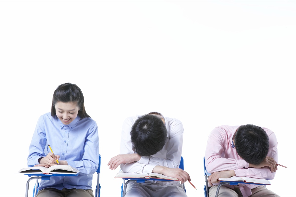 교실 책상에 앉은 학생 세 명, 한 명은 바르게 앉고 두 명은 책 위에 엎드려 있다