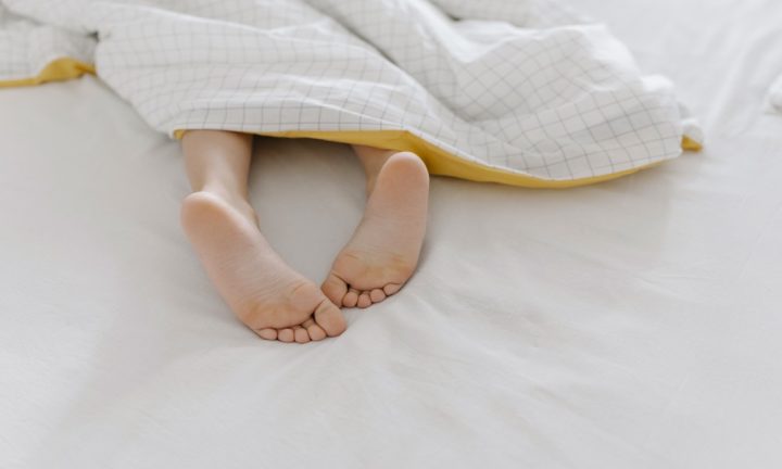 침대 이불 밖으로 나온 맨발, 발톱 건강을 떠올리게 하는 장면